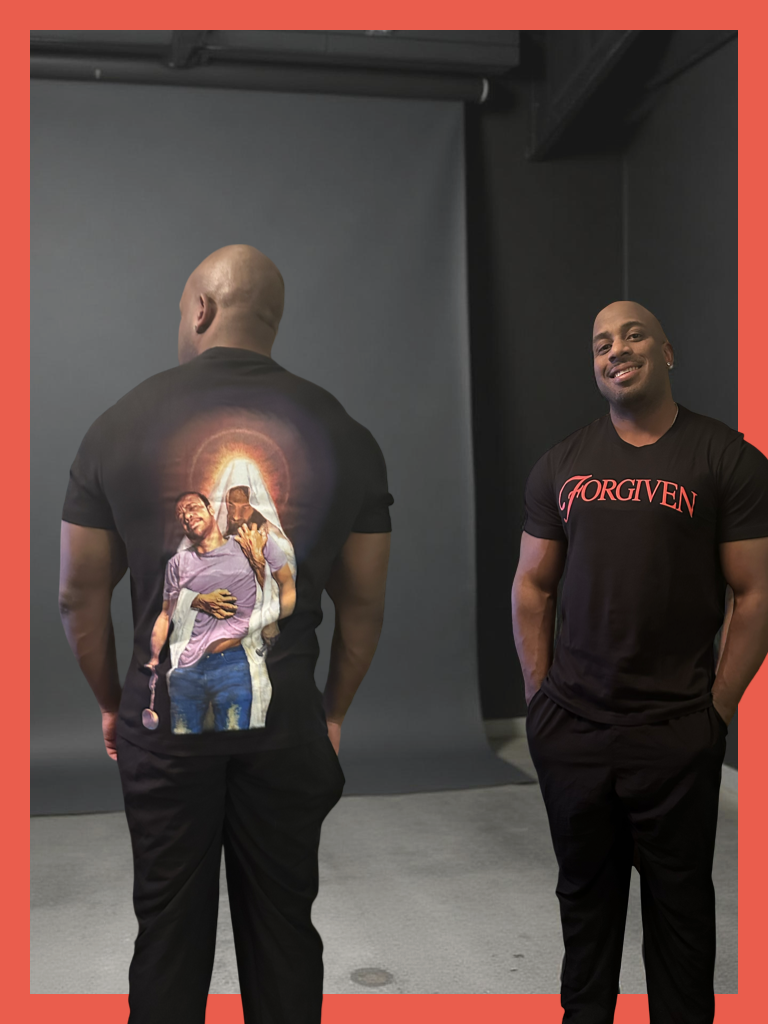 Man wearing a black t-shirt with a graphic on the back and 'FORGIVEN' text on the front, standing against a dark background.